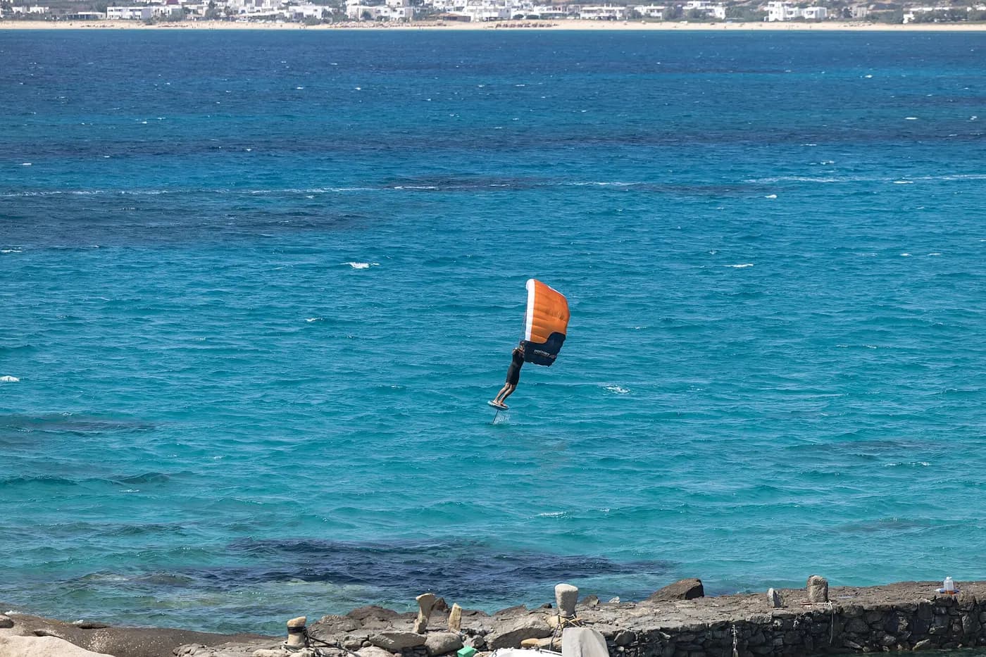 Wing foiler flying above blue water with an orange wing