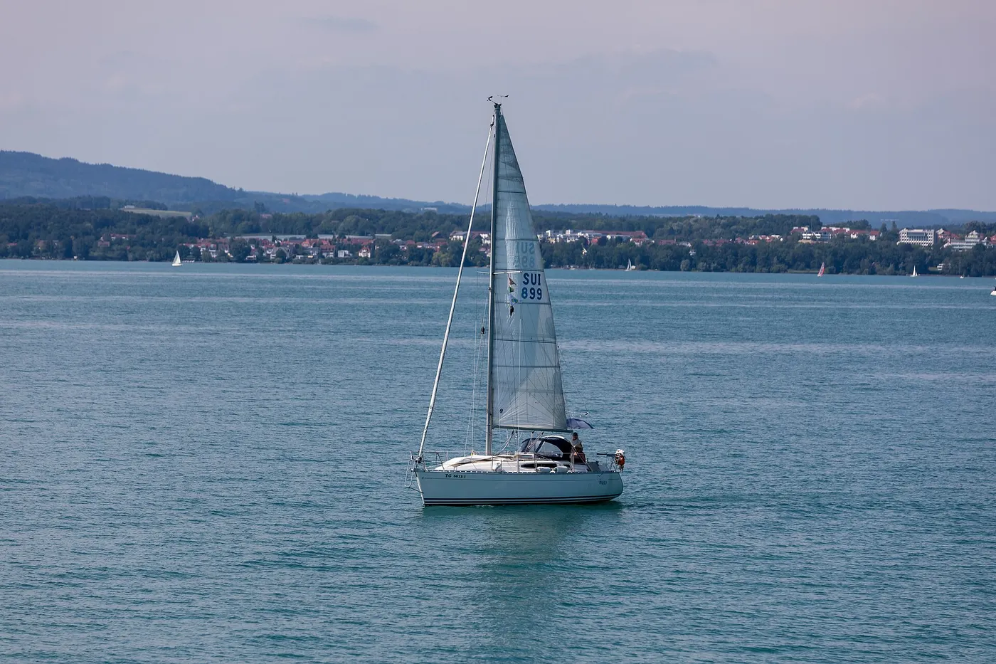 Sailboat under sail on a lake with shoreline and hills